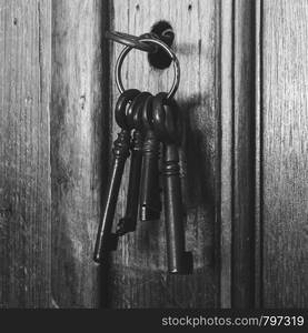 Old rusty keys inside a keyhole of an old antique closet. vintage design close-up black and white. Old rusty keys inside a keyhole of an old antique closet. vintage design black and white