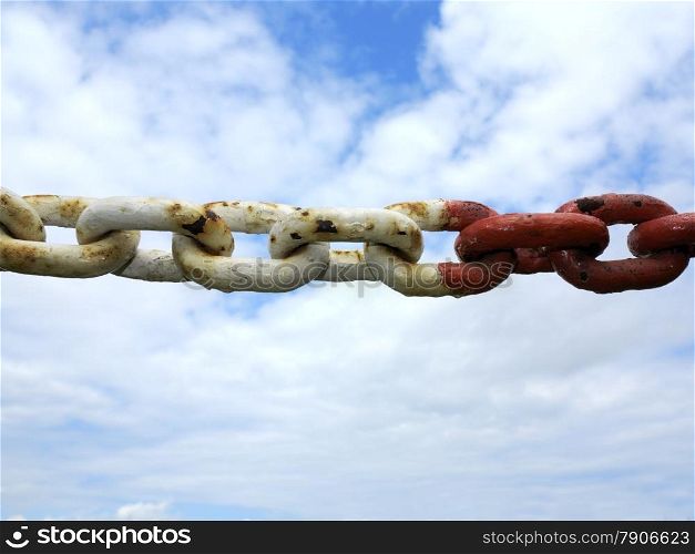 Old rusty metal steel red white chain links segment. Sky cloudy background.