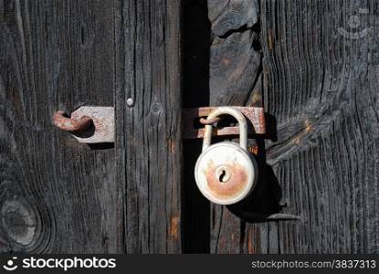 Old rusty padlock at old rough black wooden doors.