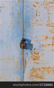 Old rusty padlock on blue weathered metal gate