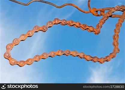 Old rusty steel chain hanging on the wire against blue sky