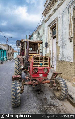 Old rusty tractor parked on city street in Cuba. Vertical view