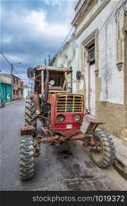 Old rusty tractor parked on city street in Cuba. Vertical view