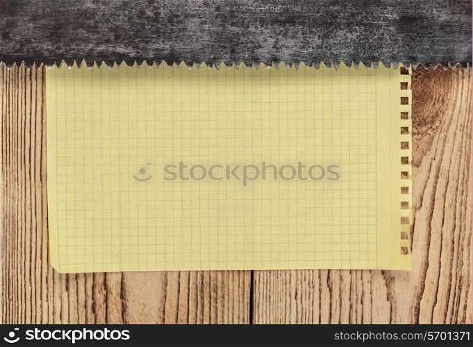 old saw and a piece of notebook on wooden background. carpentry tools on a wooden background