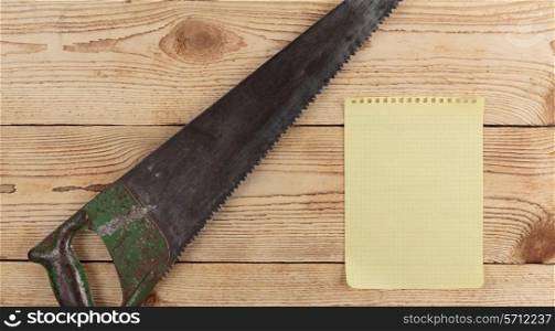 old saw and a piece of notebook on wooden background. carpentry tools on a wooden background