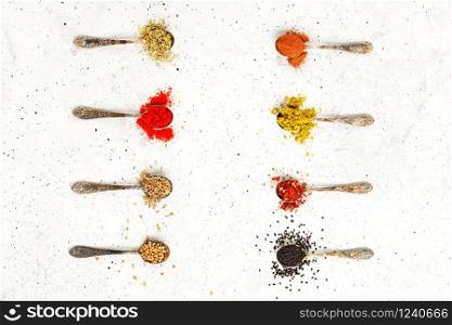 Old silver spoons with various asian spices mayran, caraway, cinnamon, hops, zira, allspice, ground paprika, corinade on a gray concrete background. Top view,, copy space.. Various seasonings in old silver spoons on a background of gray concrete.