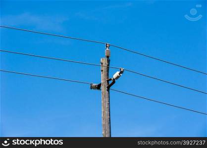 Old simple rural weathered wooden utility pole with three parallel cables and insulators against blue sky.