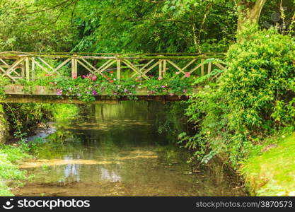 Old small bridge over river stream creek in green garden. Nature and landscape.