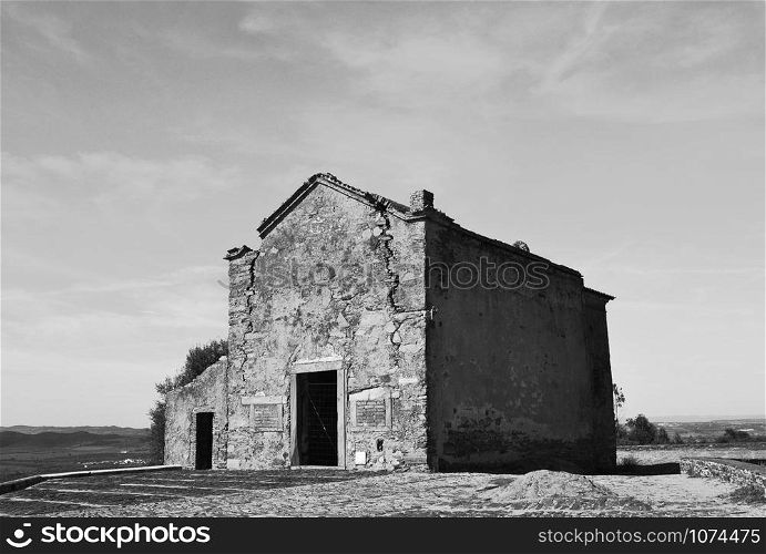 Old small building in black and white, with large cracks that mark the passage of time and its deterioration