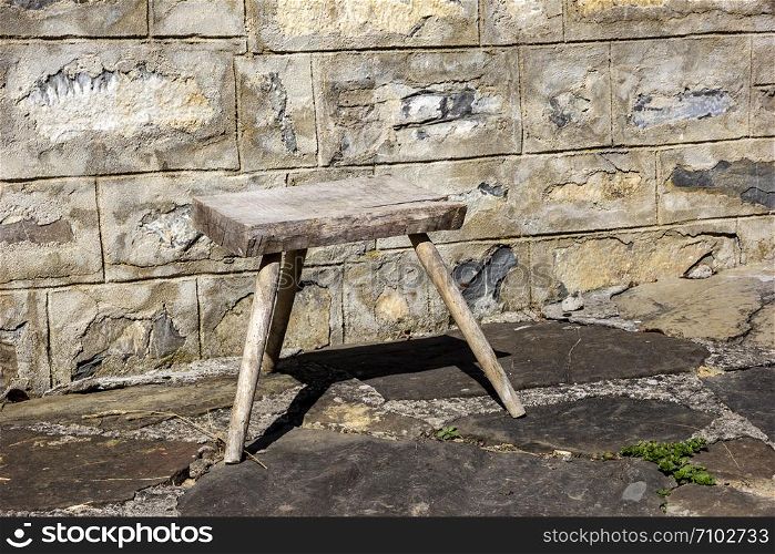 Old small wooden chair in the rural yard near a stone wall.