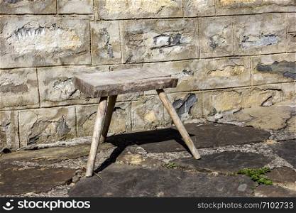 Old small wooden chair in the rural yard near a stone wall.