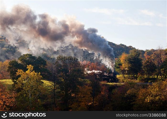 Old steam locomotive pulls freight through rural countryside in autumn