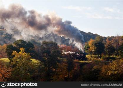 Old steam locomotive pulls freight through rural countryside in autumn