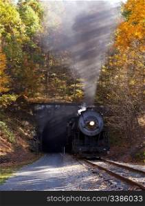 Old steam train pulling out of a tunnel belching steam and smoke
