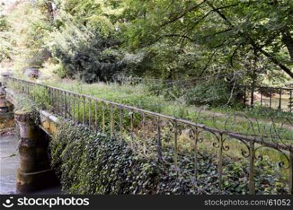 Old stone bridge with forged gates . Old stone bridge with forged gates overgrown with ivy on a river in a forest of the Meuse in France