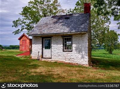 Old stone white washed cottage on farmland with trees and plants in the background. Slate roof