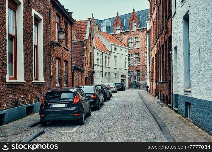 Old town Brugge street with cobblestone road with parked cars and old medieval houses. Bruges, Belgium. Brugge street with cobblestone road with parked cars and old medieval houses. Bruges, Belgium