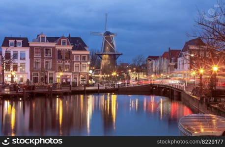 Old traditional Dutch windmill in the historical part of Leiden. Netherlands.. An old wooden mill on the banks of a canal in Leiden at dawn.