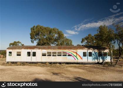 Old train carriage in the desert with a rainbow painted on it