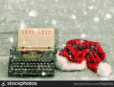 Old typewriter with red hat and sample text Wish List. Retro style picture with falling snow effect
