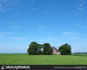 old typical farm between protecting trees under blue sky in the coutryside just outside city of leeuwarden in the netherlands