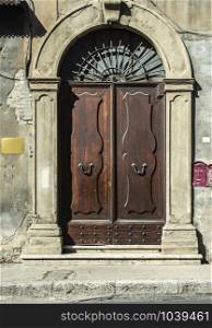 Old typical italian wooden door. Italian house. Ancient house facade. Sunlight. Round door arch. Stone build house. Wrought iron door handles.