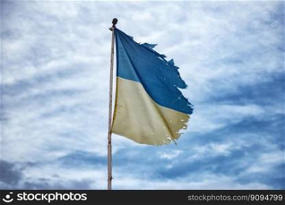 Old Ukrainian flag against the blue sky. Ukrainian tattered flag hangs on an iron pole. Waving a fabric flag in the wind. flag of the country of Ukraine close-up.