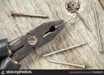 Old used pliers with nails on wood table background