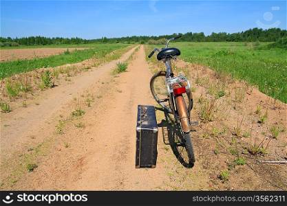 old valise near old bicycle on rural road