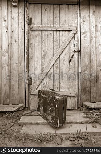 old valise near wooden door, sepia