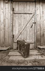 old valise near wooden door, sepia