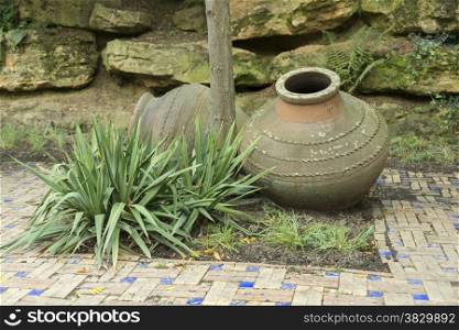 old vase and gren plant with rocks as background in garden
