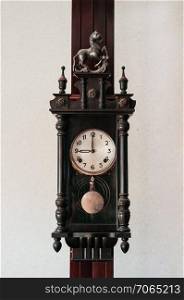 Old vintage carved dark wood grandfather wall clock hanging on wood pillar white wall background