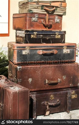 Old vintage retro used leather suitcases stacked and placed one on another in house backyard