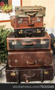 Old vintage retro used leather suitcases stacked and placed one on another in house backyard