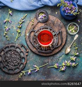 Old vintage tea setting with cup of herbal tea and fresh healing herbs and wild flowers on dark rustic background, top view. Healthy ,healing or detox drinks concept
