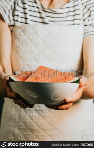 Old waitress offers and holds a watermelon in a bowl, fruits, healthy life, good eating, mediterranean concepts, copy space, vertical image, summer eating, and refreshing fruits