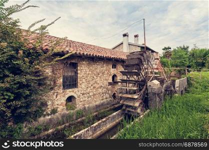 Old water mill with iron water wheel. Photo in vintage style.