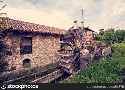 Old water mill with iron water wheel. Photo in vintage style.