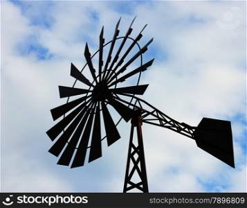 OLd water pumping windmill. Windmill water tower on sky background. Dark silhouette of farm windmill.