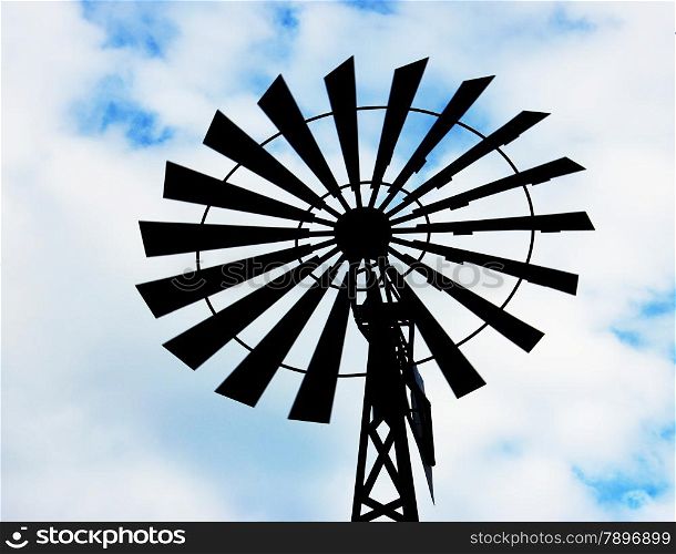 Old water pumping windmill. Windmill water tower on sky background. Dark silhouette of farm windmill.
