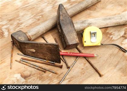 Old weathered grunge hammer, adze, measuring tape, carpenter&rsquo;s pencil and rusty nails closeup on plywood surface