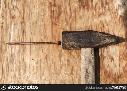 Old weathered grunge hammer and rusty nail on plywood surface as background