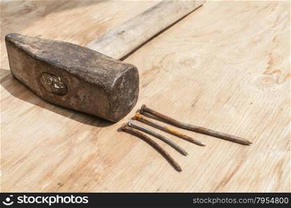 Old weathered grunge hammer and rusty nails on plywood surface as background