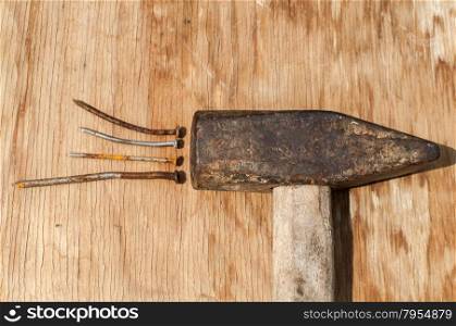 Old weathered grunge hammer and rusty nails on plywood surface as background