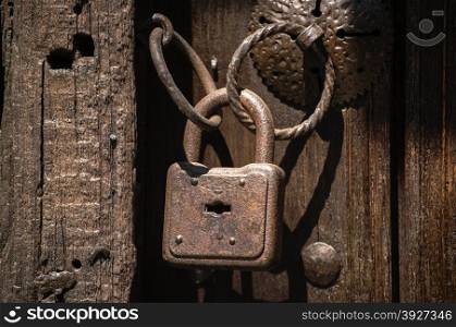 Old weathered grunge rusty locked padlock with rings on old wooden board door