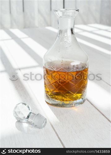 Old whisky decanter standing on a white wood table.