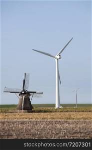 old windmill and modern turbines together in agricultutre landscape of friesland in the netherlands