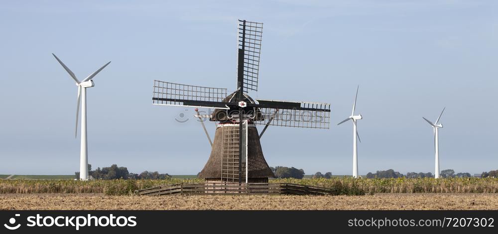 old windmill and modern turbines together in agricultutre landscape of friesland in the netherlands