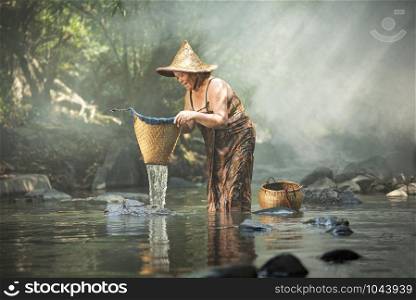 Old woman asian citizen grandmother elderly serious shower and fishing with bamboo basket on river stream nature in countryside of living life senior woman farmer rural people